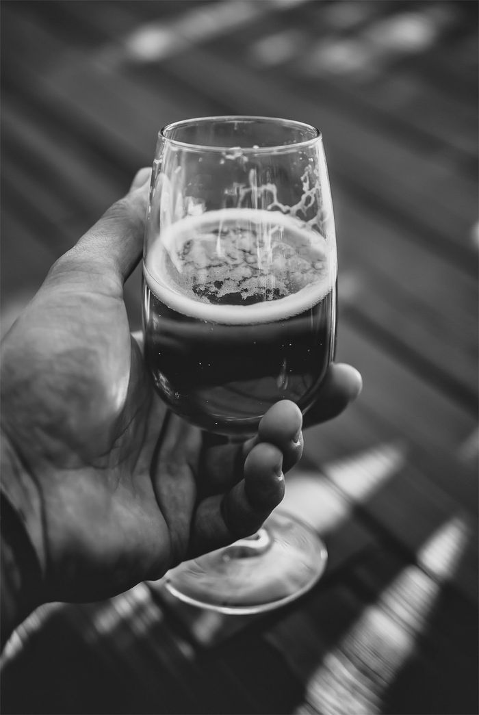 A black and white image focusing on a hand holding a glass of beer, capturing the texture and contrast.